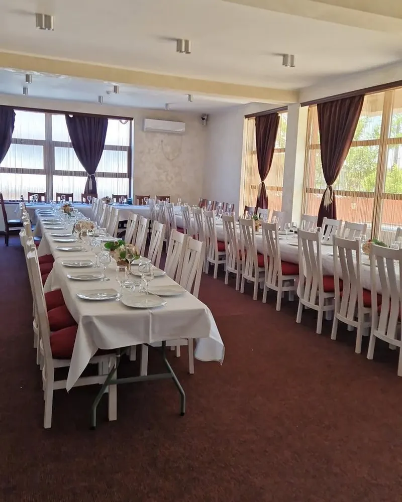 Sala de evenimente cu mese lungi, fețe de masă albe și scaune albe