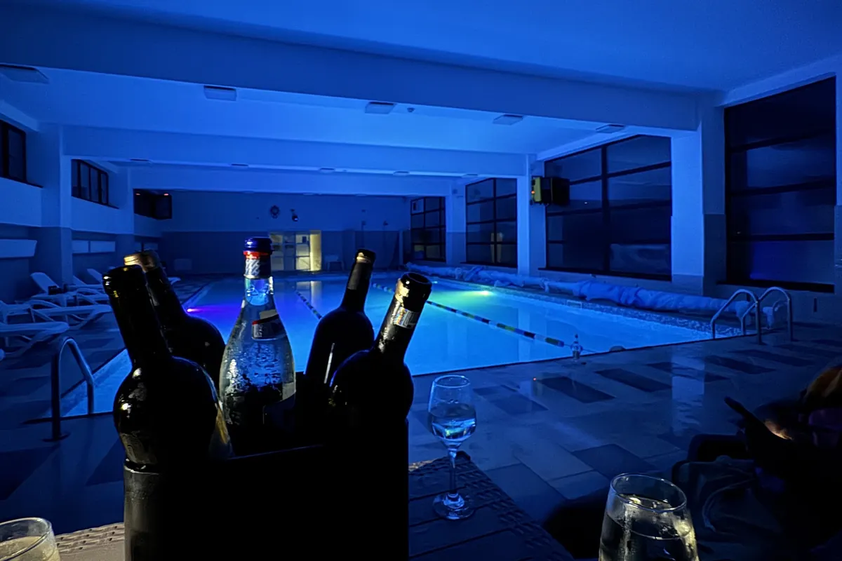 Masă cu sticle și pahare pe marginea piscinei luminate în albastru