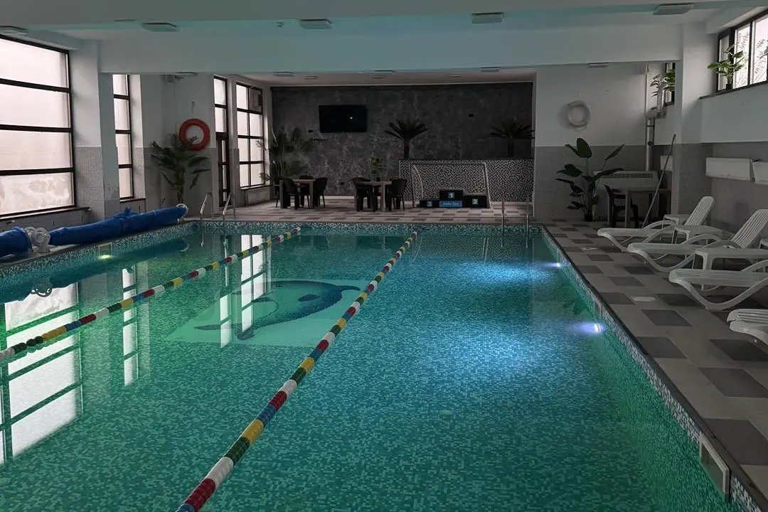 Piscina acoperită văzută din capăt, cu șezlonguri albe pe dreapta