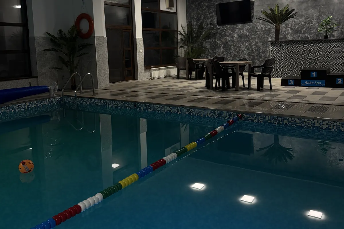 Piscina seara, cu luminile din apă aprinse și mesele de lângă bazin